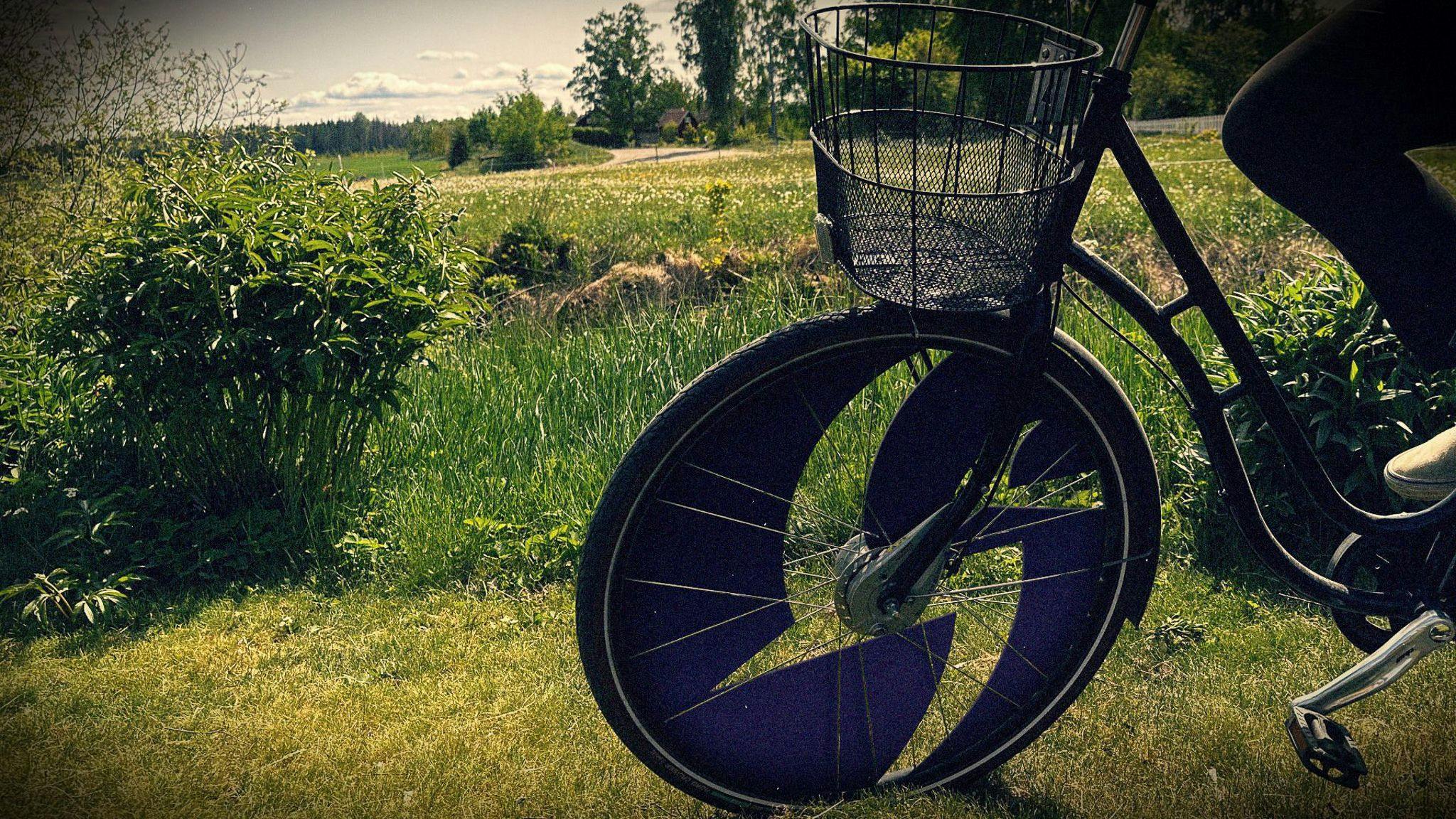 A bicycle with a wheel shaped like the Liquid Swords logo stands on a path by a field.