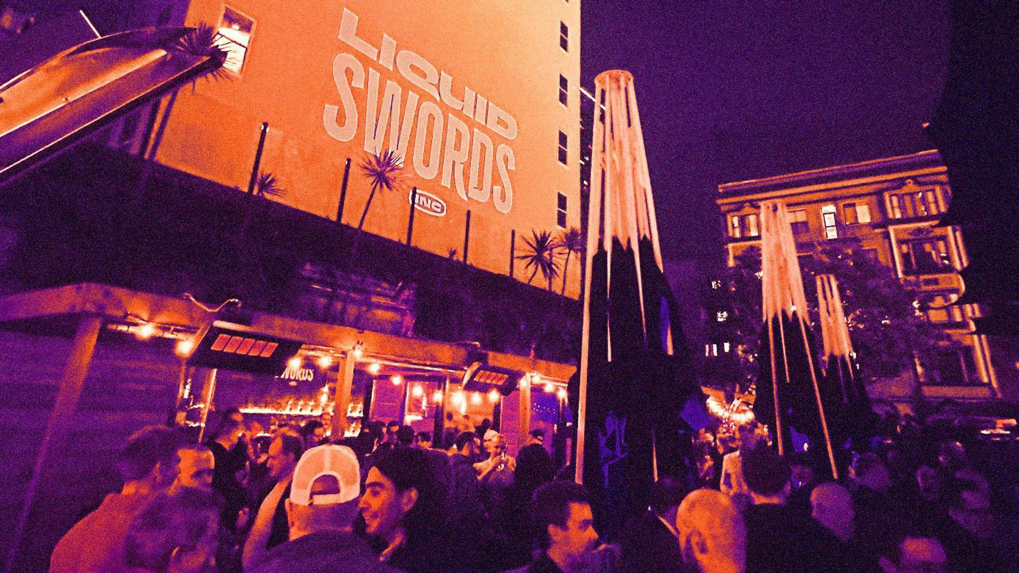 A crowd stans in front of a sign reading Liquid Swords, photo has an orange and purple treatment