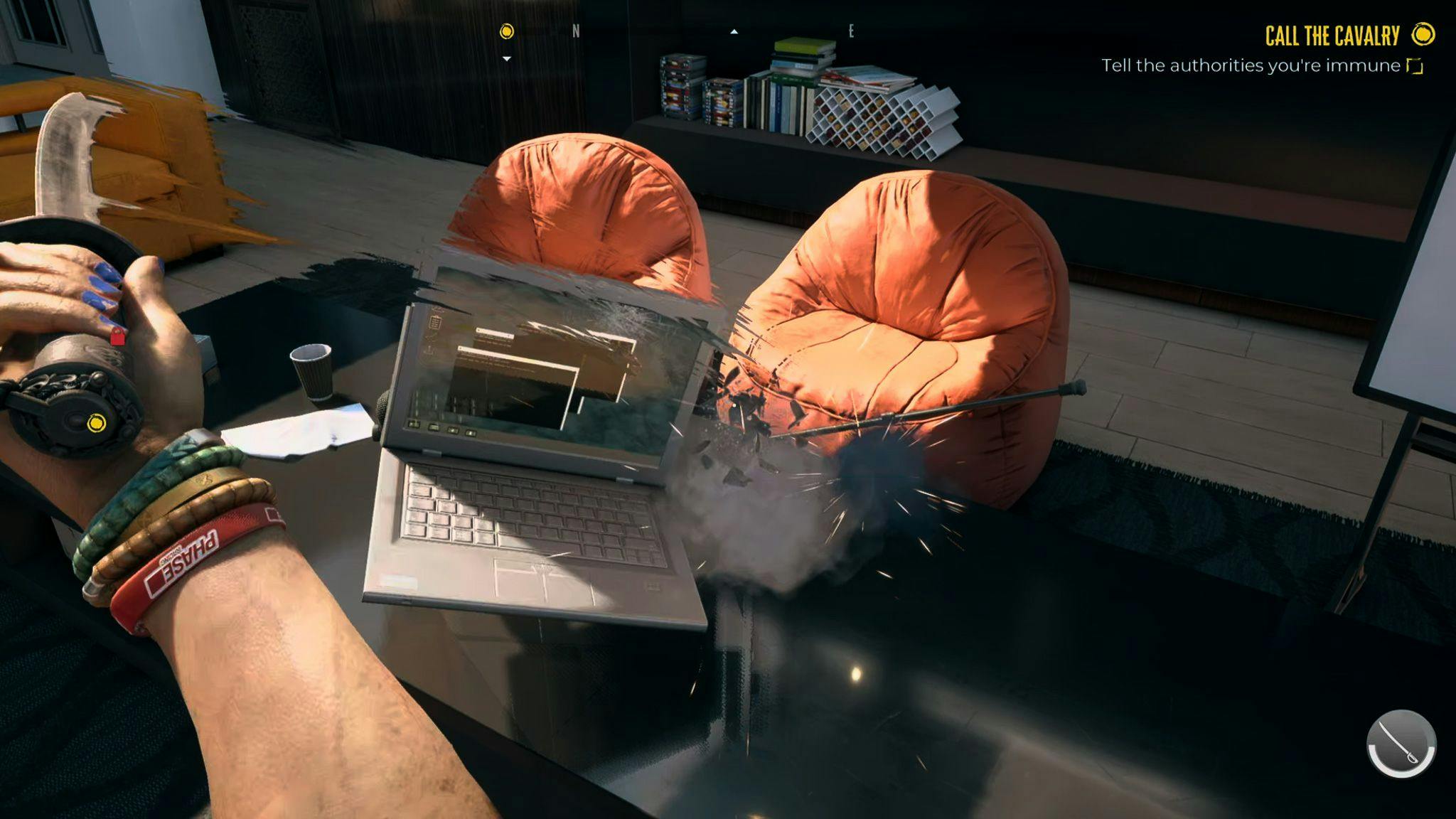 A screenshot from Dead Island 2 depicting a hand holding a sword slicing a laptop. Two orange armchairs in the background.